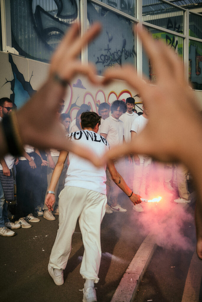 Due mani formano un cuore che inquadra un ragazzo con un fumogeno rosa davanti al gruppo ShowLove