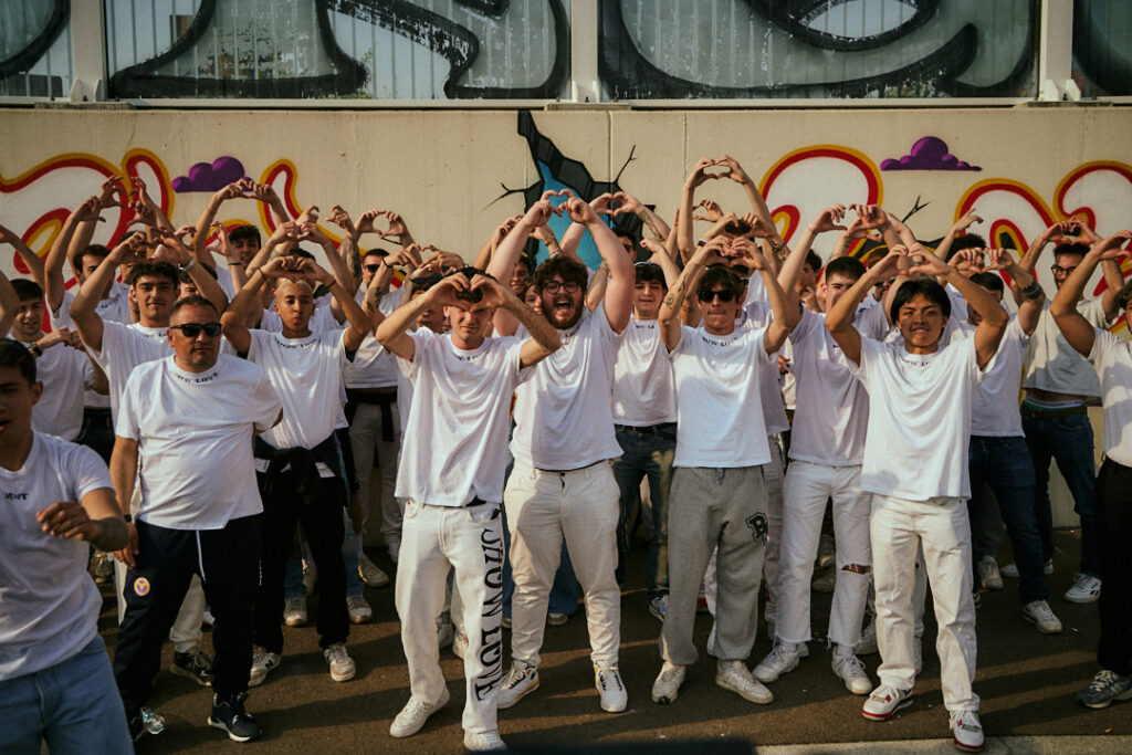 Decine di ragazzi in maglietta bianca fanno il cuore con le mani davanti al graffito ShowLove