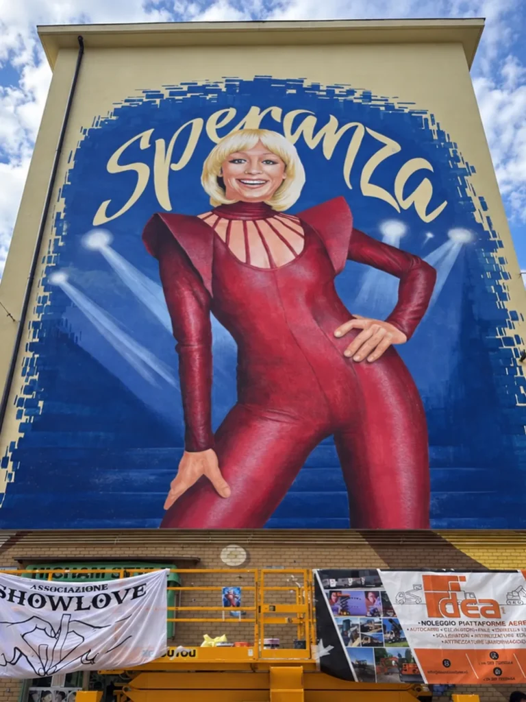 Il murale Speranza dedicato a Raffaella Carrà: Raffaella in tuta rossa su fondo blu, sulla facciata di un palazzo