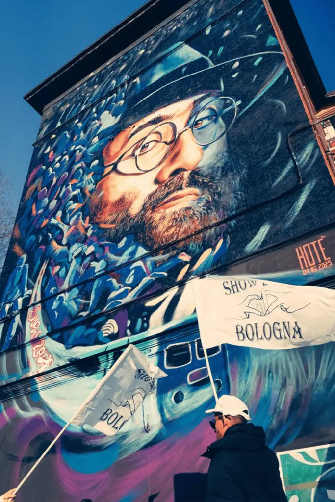 Il murale di Lucio Dalla con cappello e occhiali, con le bandiere ShowLove Bologna in primo piano